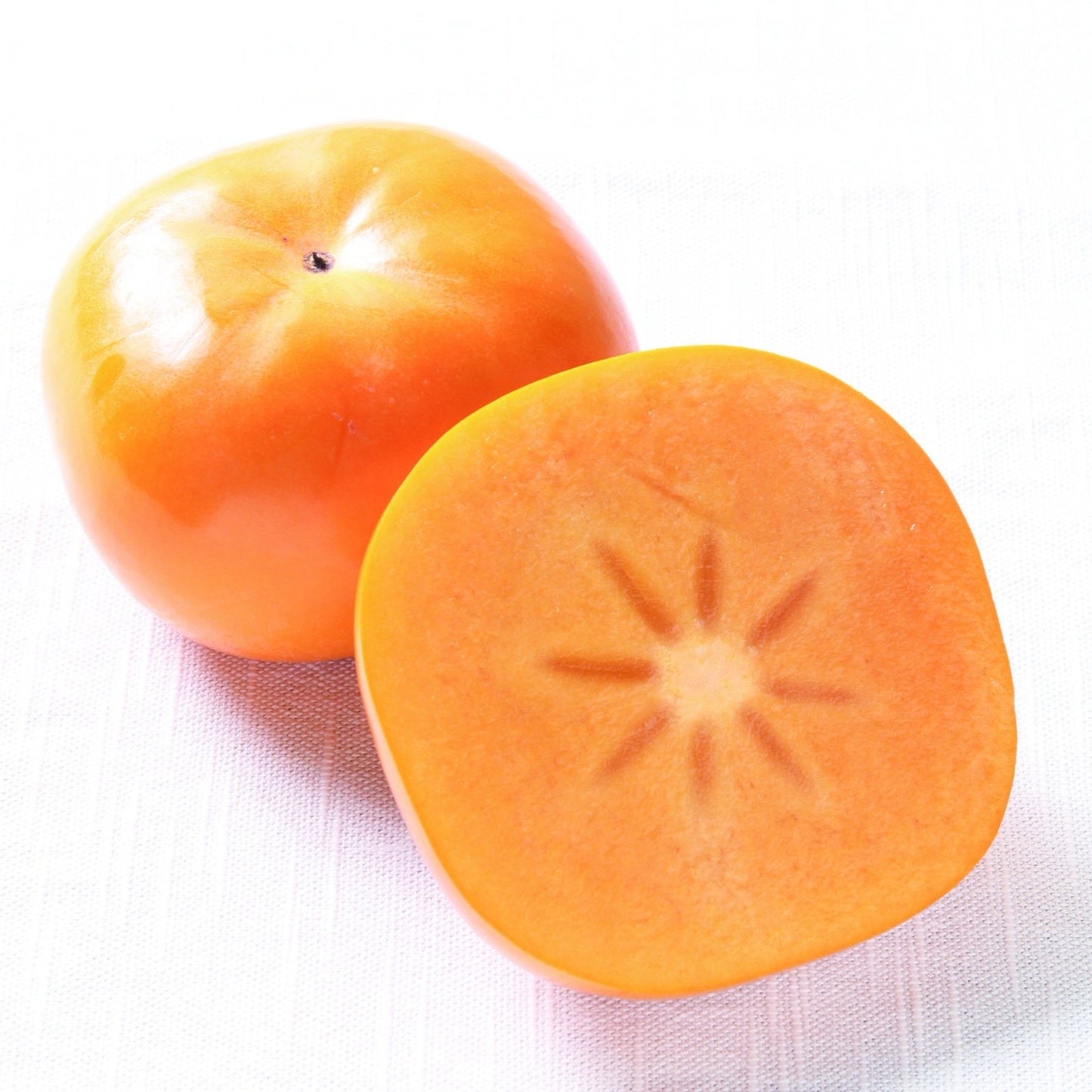 Whole Akiou persimmon beside a cut half showing its orange flesh on a white background
