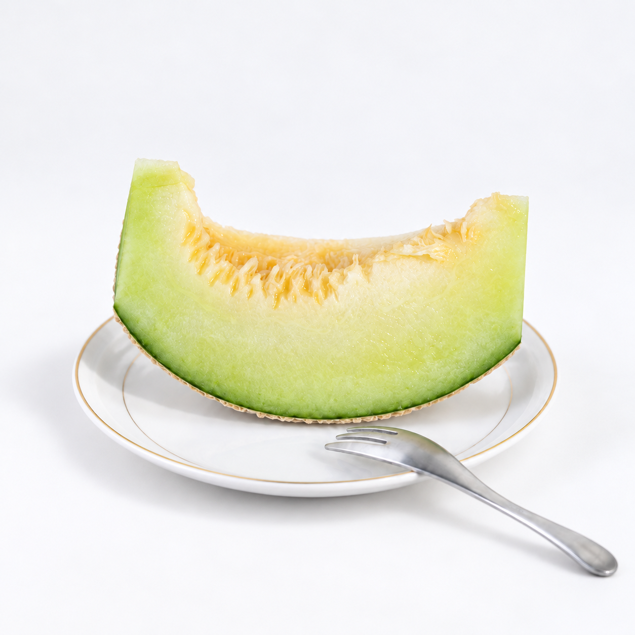 
                  
                    Fresh slice of Japanese green flesh melon with juicy pale green flesh, elegantly presented on a white plate.
                  
                